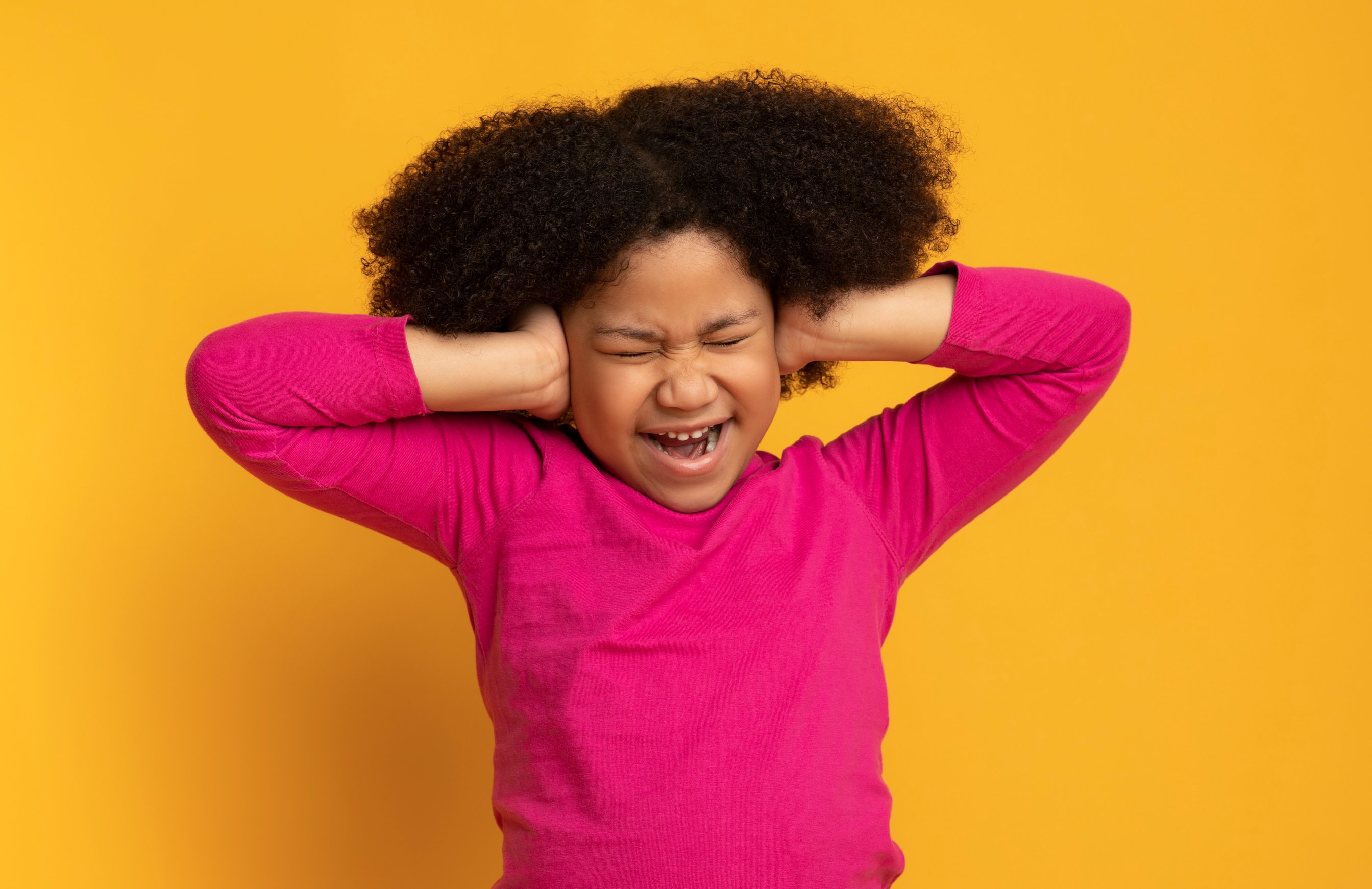 Portrait of annoyed little african girl covering ears with hands